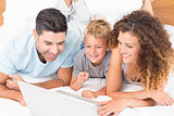 Smiling young family using laptop together on bed