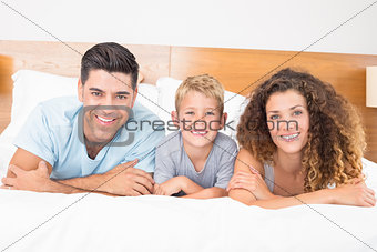 Happy young family lying on bed looking at camera