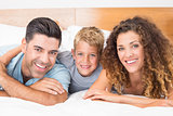 Smiling young family lying on bed looking at camera