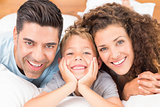 Cute young family lying on bed together smiling at camera