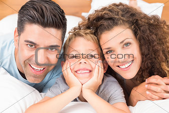 Cute young family lying on bed together smiling at camera