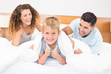 Cute young family messing about on bed with little boy showing thumbs up