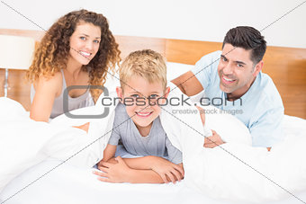 Cute young family smiling at camera on bed