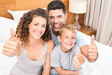 Happy young family smiling at camera on bed giving thumbs up