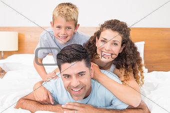 Cute young family smiling at camera on bed posing