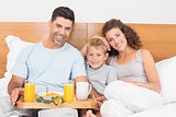 Happy young family having breakfast in bed