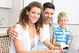 Cute little boy using laptop with parents at table