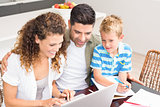Cute little boy using laptop with his parents at table