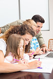 Attractive parents colouring and using laptop with their children