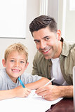 Happy father and son sitting at table colouring together