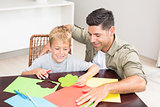 Father and son making paper shapes together at the table