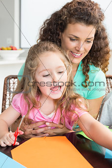 Cheerful little girl doing arts and crafts with mother at the table