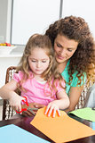 Cheerful little girl cutting paper with mother at the table