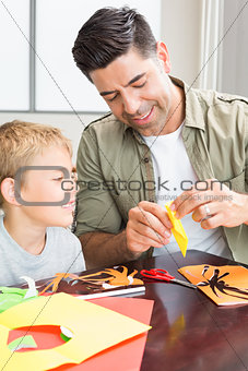 Cheerful little boy making paper shapes with father at the table