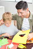 Little boy making paper shapes with father at the table