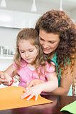 Little girl making paper shapes with mother at the table