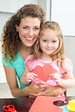 Cute little girl showing paper heart sitting on mothers lap