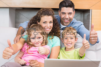 Happy family sitting on sofa using laptop giving thumbs up