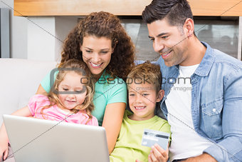 Happy family sitting on sofa using laptop together to shop online