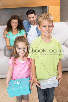 Siblings holding presents in front of parents on the couch