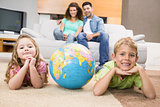 Smiling siblings lying on the rug with a globe