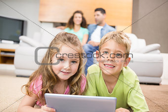 Happy siblings lying on the rug using a tablet