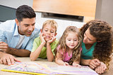 Cute siblings lying on the rug reading storybook with their parents