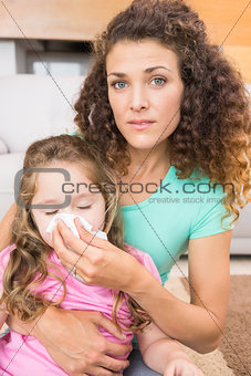 Worried mother helping her little daughter blow her nose