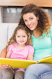Pretty mother sitting with her little daughter reading a storybook