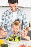 Smiling father tossing salad with his son