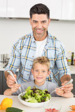 Smiling father tossing salad with his cute son