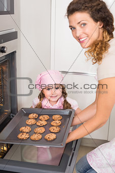 Mother taking cookies out of the oven with daughter