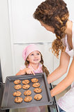 Mother taking cookies out of the oven with daughter pointing at one