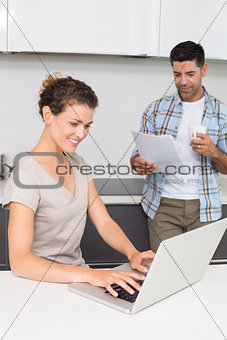 Happy woman using laptop while partner reads the newspaper