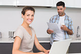 Cheerful woman using laptop while partner reads the newspaper