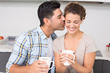 Happy woman drinking coffee getting a kiss from partner