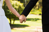 Mid section of newlywed couple holding hands in park