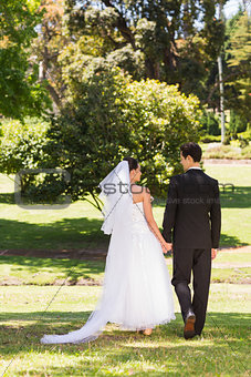 Rear view of newlywed couple walking in park