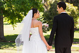 Newlywed couple holding hands and walking in park