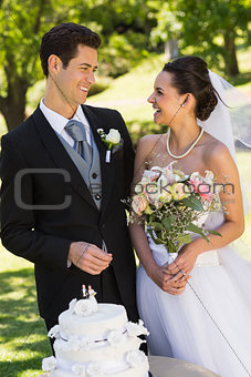 Newlywed couple with wedding cake at park
