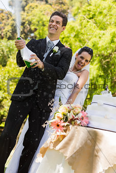 Newlywed couple with groom opening champagne bottle at park