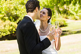 Newlywed kissing while toasting champagne flutes at park