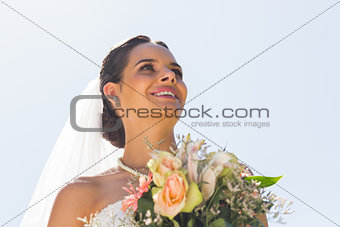 Smiling beautiful bride with bouquet against clear sky
