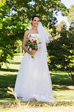 Smiling young beautiful bride with bouquet in park