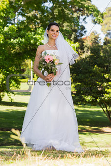 Smiling young beautiful bride with bouquet in park