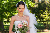 Serious beautiful bride with bouquet in park
