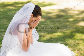 Beautiful worried bride sitting at park