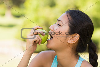 Healthy young woman eating apple in park