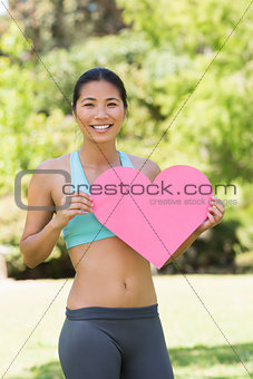 Smiling woman holding heart shape board in park