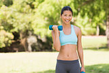 Healthy smiling woman exercising with dumbbells in park